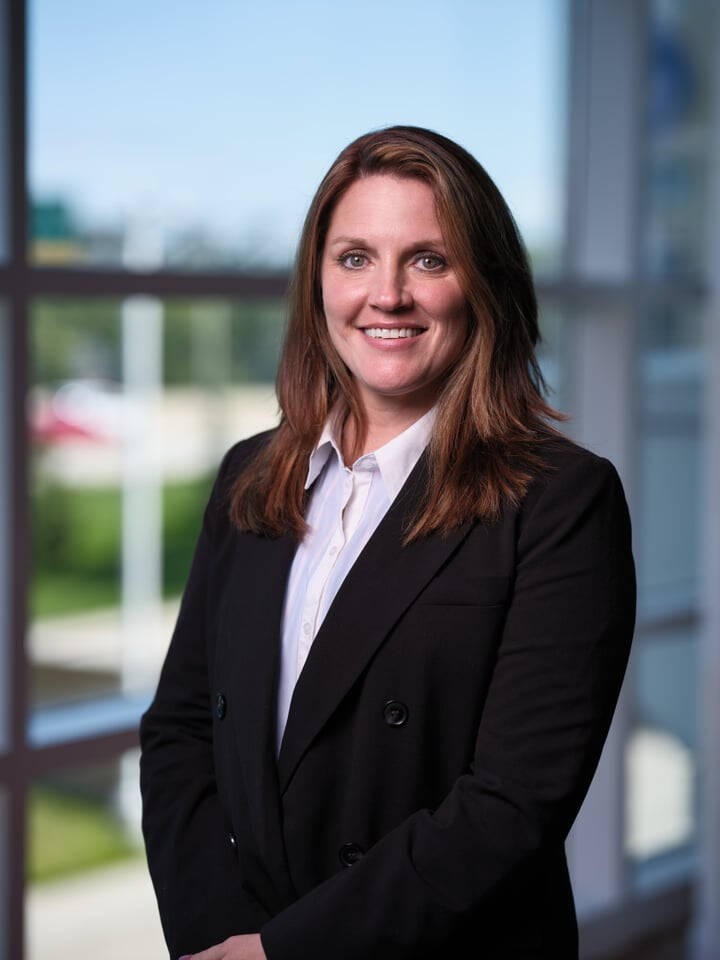 Brianne smiles at the camera wearing a black blazer and white collared shirt